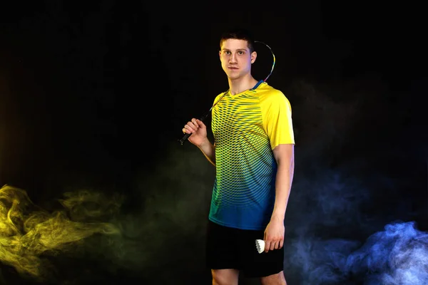 Badminton player in sportswear with racket and shuttlecock on black background with color smoke. Olympic game. — Stock Photo, Image