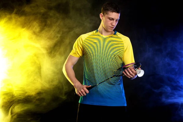 Badminton player in sportswear with racket and shuttlecock on black background with color smoke. Olympic game. — Stock Photo, Image