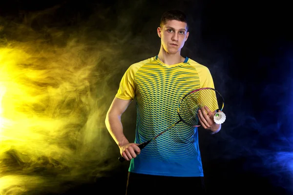 Badminton player in sportswear with racket and shuttlecock on black background with color smoke. Olympic game. — Stock Photo, Image