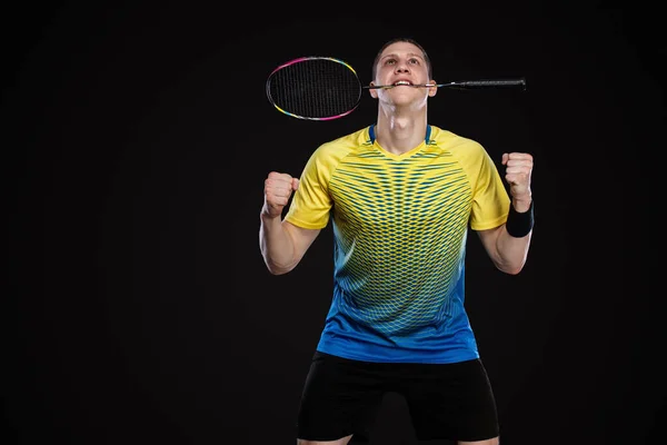 Badminton w odzieży sportowej z rakietą i wahadłowcem na czarnym tle. Człowiek świętuje zwycięstwo na ciemnym tle. Gry Olympic gry. — Zdjęcie stockowe
