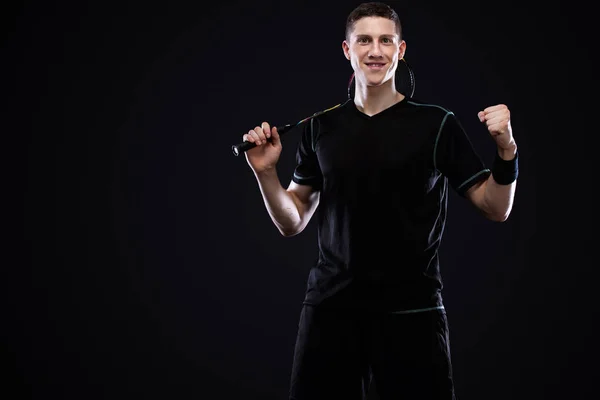 Joueur de badminton en tenue de sport avec raquette et volant sur fond noir. L'homme célèbre la victoire sur le fond sombre avec . — Photo