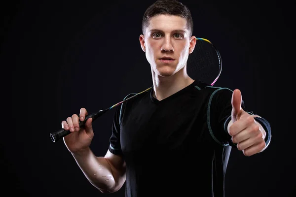 Badminton player in sportswear with racket and shuttlecock on black background. Emotional sport portrait with man which show sight thumbs up and good luck. — Stock Photo, Image