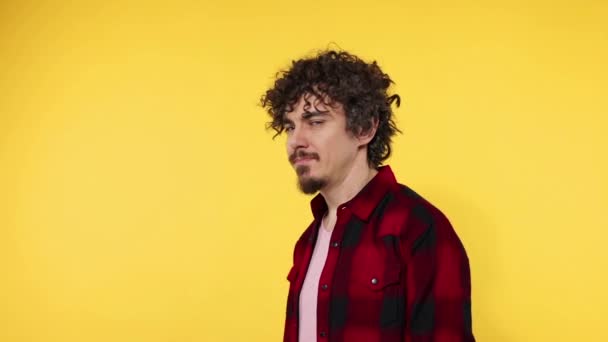 Retrato de primer plano del chico feliz sonriente con el pelo rizado mirando a la cámara aislada sobre fondo amarillo. El tipo señala con el dedo a la cámara — Vídeos de Stock