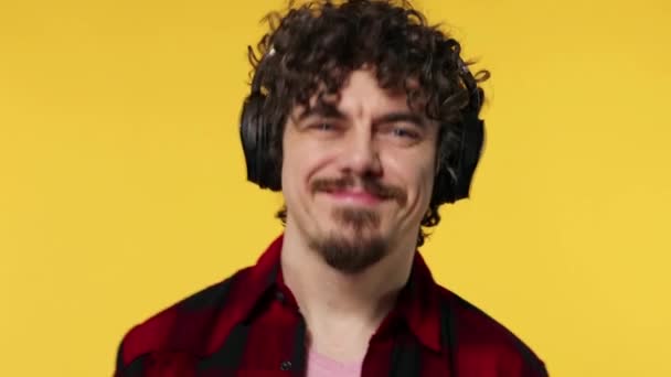 Schöner glücklicher europäischer Mann mit Bart im roten Hemd lächelt und tanzt isoliert auf gelbem Hintergrund. Kerl mit Kopfhörer hört Musik. Lifestyle-Konzept. — Stockvideo