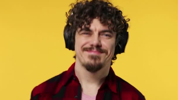 Guapo hombre europeo feliz con barba en camisa roja sonriendo y bailando aislado sobre fondo amarillo. Un tipo con auriculares escuchando música. Concepto de estilo de vida . — Vídeos de Stock