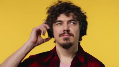 Handsome happy european man with beard in red shirt smiling and dancing isolated on yellow background. Guy in headphones listening to music. Lifestyle concept.