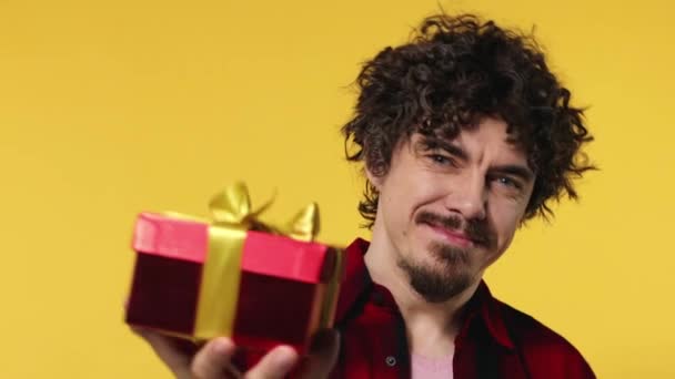 A man gives a red gift for Valentines Day or International Womens Day. Birthday surprise. Handsome happy european man with beard in shirt smiling isolated on yellow background. — Stok video