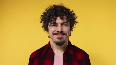 Handsome happy european man with curly hair shakes his head. Guy with beard and mustache in red shirt smiling and dancing isolated on yellow background. Lifestyle concept. Slow motion.
