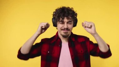 Handsome happy european man with beard in red shirt smiling and dancing isolated on yellow background. Guy in headphones listening to music. Lifestyle concept. Slow motion.