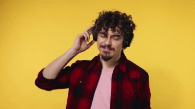 Handsome happy european man with beard in red shirt smiling and dancing isolated on yellow background. Guy in headphones listening to music. Lifestyle concept. Slow motion.