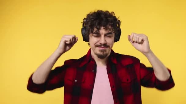 Handsome happy european man with beard in red shirt smiling and dancing isolated on yellow background. Guy in headphones listening to music. Lifestyle concept. Slow motion. — Stock Video