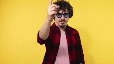 Man shows thumbs up sign with fingers. Closeup portrait of happy smiling guy with curly hair looking at camera isolated on yellow background. Slow motion.