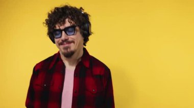 Handsome happy european man with beard in red shirt smiling and dancing isolated on yellow background. Guy in headphones listening to music. Lifestyle concept. Slow motion.