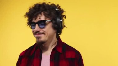 Handsome happy european man with beard in red shirt smiling and dancing isolated on yellow background. Guy in headphones listening to music. Lifestyle concept. Slow motion.