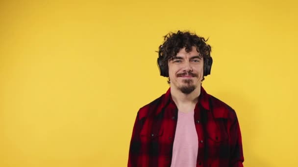Man shows thumbs up sign with fingers. Closeup portrait of happy smiling guy with curly hair looking at camera isolated on yellow background. Slow motion. — 비디오