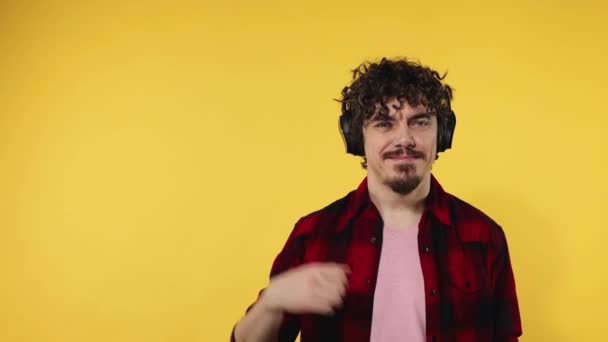 Man shows ok sign with fingers. Closeup portrait of happy smiling guy with curly hair looking at camera isolated on yellow background. Slow motion. Model pointing to looking left on copy space. — Stok video