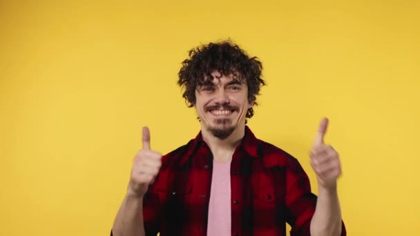 Muž ukazuje ukazováček prstem nahoru. Detailní portrét šťastného usmívajícího se chlapa s kudrnatými vlasy při pohledu do kamery izolované na žlutém pozadí. Zpomalený pohyb. — Stock video