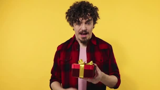 A man gives a red gift for Valentines Day lovers or International Womens Day. Birthday surprise. Handsome happy european man with beard in shirt smiling isolated on yellow background. Slow motion. — Stock Video