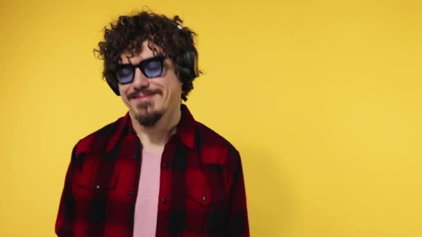 Handsome happy european man with beard in red shirt smiling and dancing isolated on yellow background. Guy in headphones listening to music. Lifestyle concept. Slow motion. — Stok video