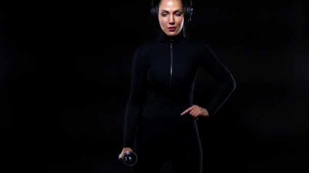 Sport and fitness concept. Fit woman athlete in sportswear and headphones working out with dumbbells. Girl isolated over black background. — Stock Video