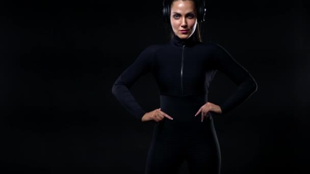 Sport- und Fitnesskonzept. Fitte Sportlerin in Sportbekleidung und Kopfhörer beim Training. Mädchen isoliert über schwarzem Hintergrund. — Stockvideo