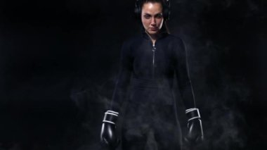 Spor salonunda boks antrenmanı yapan genç kadın sporcu boksör. Eldiven giyen, spor kıyafetler giyen ve kum torbasına vuran kız. Duman ile siyah arka plan üzerinde izole. Kopyalama Alanı.