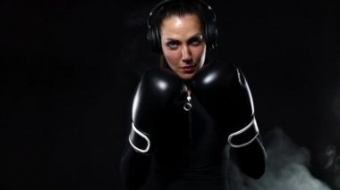 Genç bayan sporcu boksör spor salonunda boks antrenmanı yapıyor. Eldiven giyen, spor giyinen ve kum torbasına vuran bir kız. Siyah arka planda dumanla izole edilmiş. Yavaş çekim,