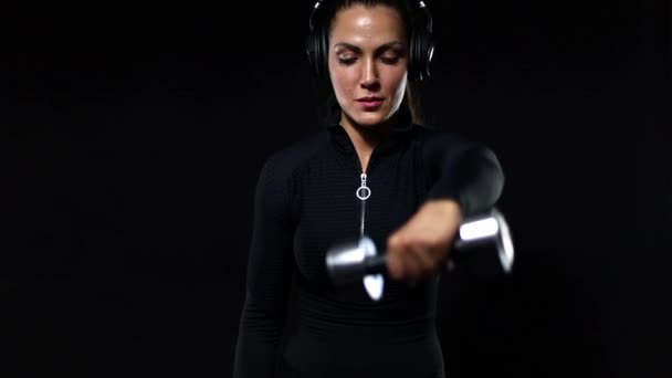 Concepto de deporte y fitness. Ajuste mujer atleta en ropa deportiva y auriculares que trabajan con pesas. Chica aislada sobre fondo negro. Movimiento lento , — Vídeo de stock