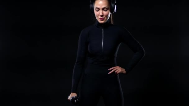 Sport en fitness concept. Fit vrouwelijke atleet in sportkleding en koptelefoon uit te werken met halters. meisje geïsoleerd over zwart achtergrond. — Stockvideo