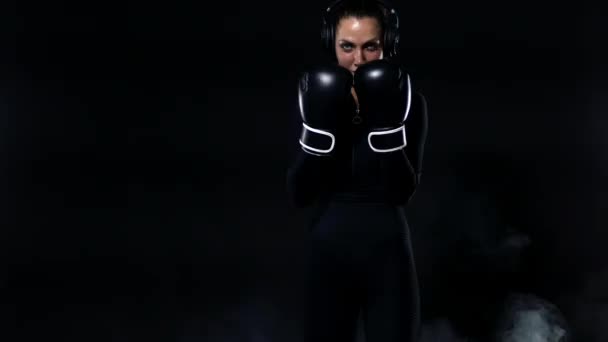 Mujer joven deportista boxeadora haciendo entrenamiento de boxeo en el gimnasio. Chica con guantes, ropa deportiva y golpear el saco de boxeo. Aislado sobre fondo negro con humo. Copiar espacio . — Vídeos de Stock