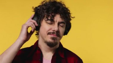 Handsome happy european man with beard in red shirt smiling and dancing isolated on yellow background. Guy in headphones listening to music. Lifestyle concept.