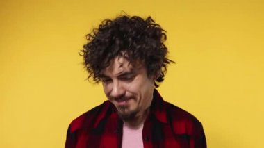 Handsome happy european man with curly hair shakes his head. Guy with beard and mustache in red shirt smiling and dancing isolated on yellow background. Lifestyle concept. Slow motion.