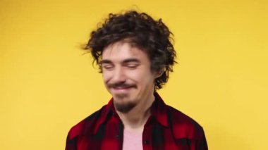 Handsome happy european man with curly hair shakes his head. Guy with beard and mustache in red shirt smiling and dancing isolated on yellow background. Lifestyle concept. Slow motion.