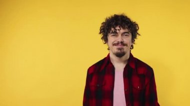 Man shows ok sign with fingers. Closeup portrait of happy smiling guy with curly hair looking at camera isolated on yellow background. Slow motion.