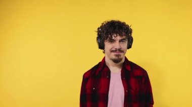 Handsome happy european man with beard in red shirt smiling and dancing isolated on yellow background. Guy in headphones listening to music. Lifestyle concept. Slow motion.