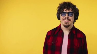 Handsome happy european man with beard in red shirt smiling and dancing isolated on yellow background. Guy in headphones listening to music. Lifestyle concept. Slow motion.