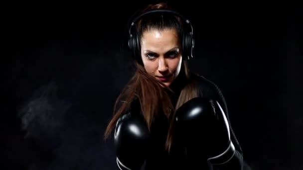 Mujer joven deportista boxeadora haciendo entrenamiento de boxeo en el gimnasio. Chica con guantes, ropa deportiva y golpear el saco de boxeo. Aislado sobre fondo negro con humo. Movimiento lento , — Vídeos de Stock