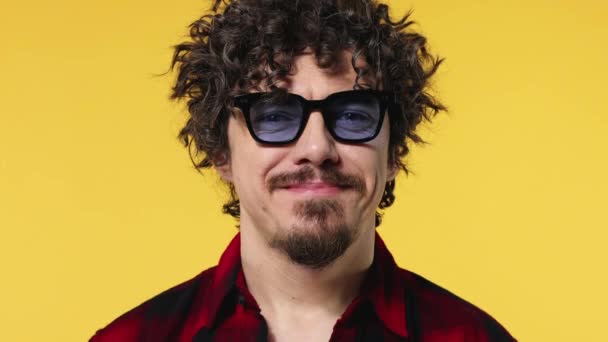 Amazed and happy european man in blue sunglasses smiling. Handsome guy with stylish curly hair isolated on yellow background. Lifestyle concept. — Stock Video