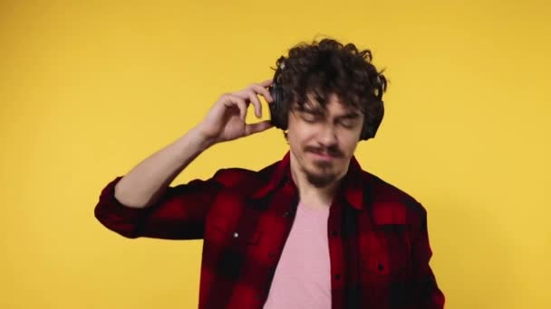 Handsome happy european man with beard in red shirt smiling and dancing isolated on yellow background. Guy in headphones listening to music. Lifestyle concept. Slow motion. — Stok video