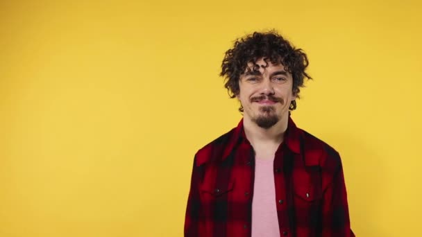 Man shows ok sign with fingers. Closeup portrait of happy smiling guy with curly hair looking at camera isolated on yellow background. Slow motion. — Stock Video