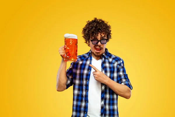 圣帕特里克日。年轻的Oktoberfest男子提供大啤酒瓶与饮料隔离黄色背景。手指头上的手势不错. — 图库照片