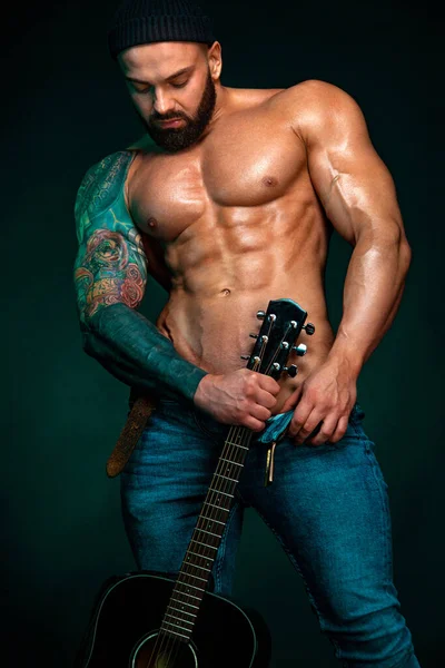 Gitarlı güçlü ve formda bir vücut geliştirici karın kasları gösteriyor. Sportif kaslı erkek atlet. Spor ve spor konsepti. Erkek modası.