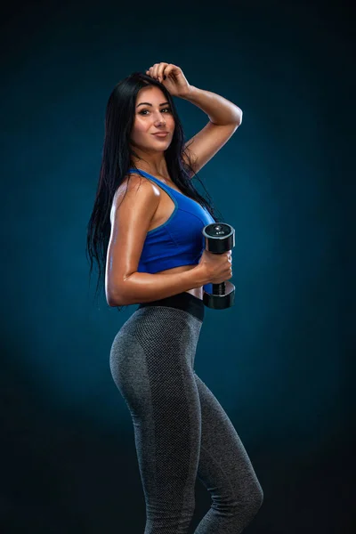 Mujer atlética fuerte con mancuernas sobre fondo oscuro con ropa deportiva azul. Fitness y motivación deportiva . — Foto de Stock