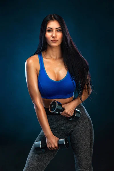 Mujer atlética fuerte con mancuernas sobre fondo oscuro con ropa deportiva azul. Fitness y motivación deportiva . — Foto de Stock