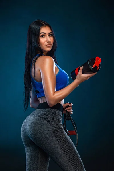 Fuerte atlética mujer en forma con agitador sobre fondo oscuro que lleva en ropa deportiva azul. Fitness y motivación deportiva . — Foto de Stock