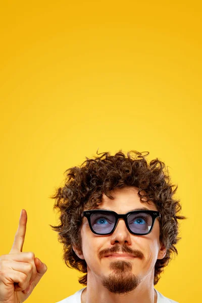 Portrait of happy bearded man with curly hair pointing finger up at copyspace isolated over yellow background. Guy in blue sunglasses pick on great idea. — Stok fotoğraf