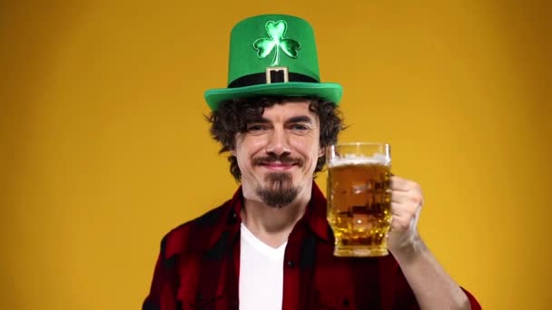 Saint Patrick Day. Young Oktoberfest man serving big beer mug with drink isolated on yellow background. Slow Motion. — Stock Video