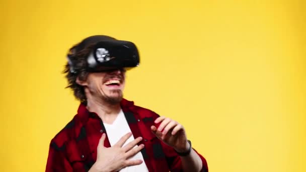 Jeune homme avec les cheveux bouclés à l'aide d'un casque VR et l'expérience de la réalité virtuelle isolé sur fond jaune — Video