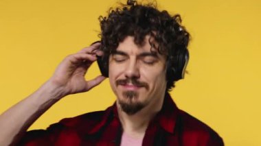 Handsome happy european man with beard in red shirt smiling and dancing isolated on yellow background. Guy in headphones listening to music. Lifestyle concept.
