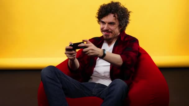 Nerdy gamer com controlador em fundo amarelo. Homem com cabelo encaracolado — Vídeo de Stock